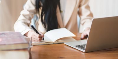 Mulher estudando com computador e caderno para uma pós graduação EAD.